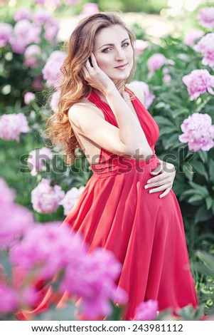 Happy pregnant woman hugging her stomach on the background of peony flowers,outdoor. Spring mood.