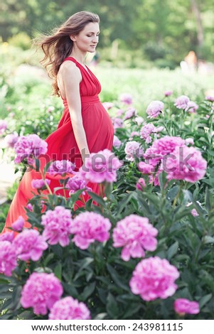 Happy pregnant woman hugging her stomach on the background of peony flowers,outdoor. Spring mood.