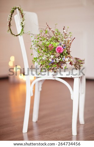 White vintage chair with candle and flowers bouquet near white wall.
