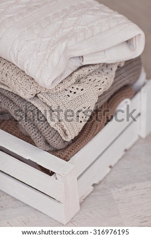 White wool sweaters in wood box on white wood floor