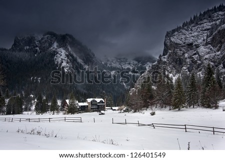 Chalet in the mountains in winter time and dark clouds covered the rocks