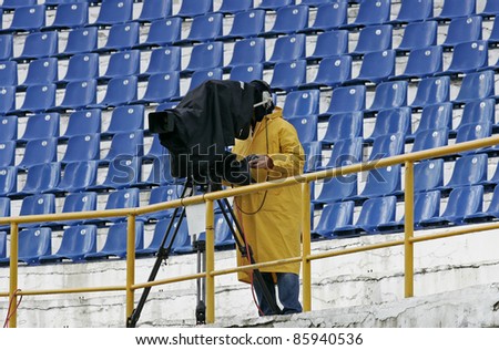 a cameraman filming a football game on a stadium in the rain