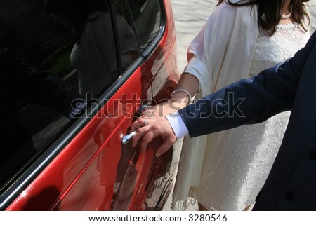 Newly-married couple near a wedding limousine, their reflection is visible in its windows