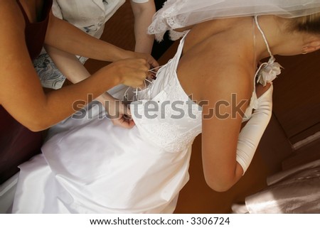 The bridesmaid and mum help the bride to tighten a corset