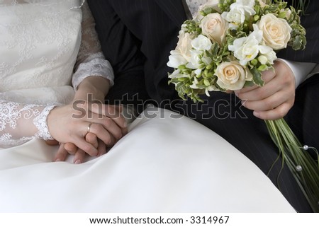 Gently connected hands of a newly-married couple with wedding rings on a finger on a background of a white wedding dress