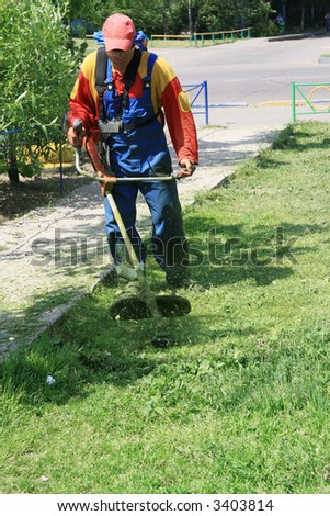 The seasonal worker in special clothes and protective eyeglass cuts a grass on a lawn