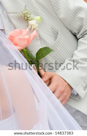 Gentle touches of hands of an enamoured newly-married couple on a background of wedding clothes