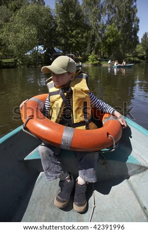 The little boy with a life jacket and a life buoy sits in a boat