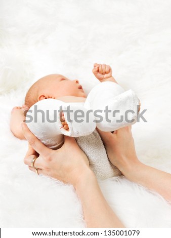 Mother holding new born baby\'s legs wrapped in bandage on fur blanket