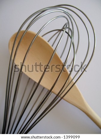 A whisk and a wooden spoon. Focused on the whisk.