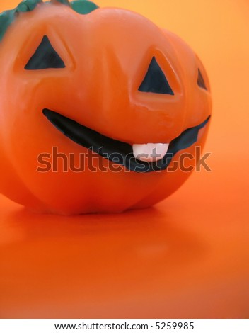 An orange smiling wax pumpkin against orange background.