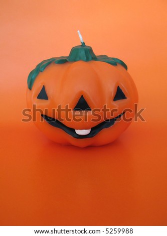 An orange smiling wax pumpkin against orange background.