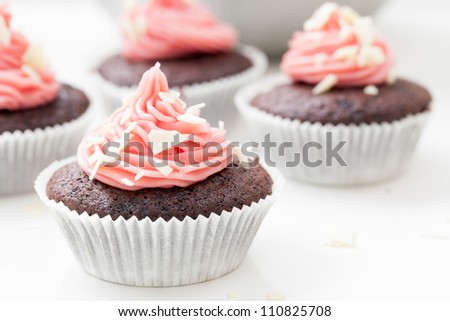 Chocolate cupcake topped with pink icing and sprinkled with white chocolate flakes.