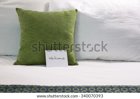 Welcoming hotel bed with pillows and welcome card close up.