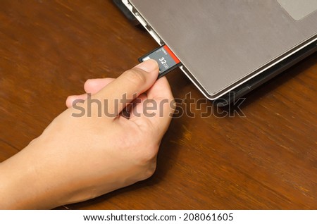 hand holding SD card insert to notebook computer