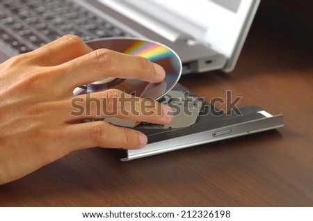 hand holding DVD insert to laptop computer
