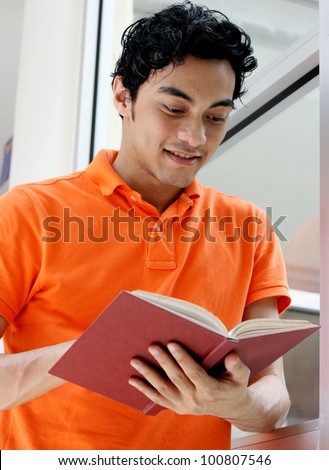 Portrait of a smiling handsome young man reading a book