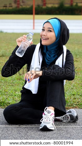 A pretty muslim woman athlete resting while drink a bottle of mineral water