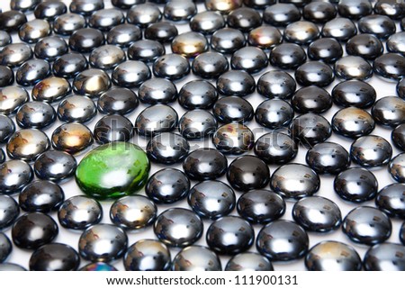 Lonely green stone among black stones in a white background