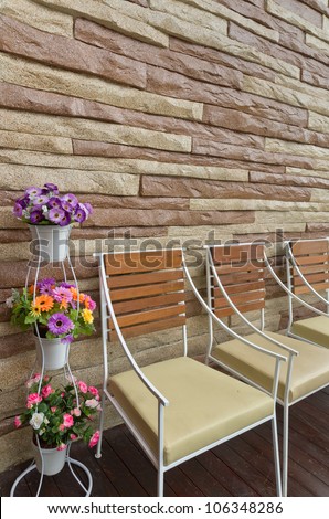 Colorful flowers in white pot wood chair and stone wall