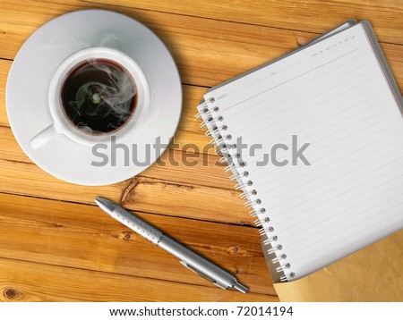 White cup of hot coffee and blank page note book on wood table with silver pen