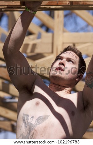 POCONO MANOR, PA - APR 29: A man moves hand-over-hand through an obstacle at Tough Mudder on April 29, 2012 in Pocono Manor, Pennsylvania. The course is designed by British Royal troops.