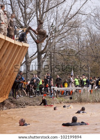 POCONO MANOR, PA - APR 28: A man does a flip off the Walk the Plank obstacle into water at Tough Mudder on April 28, 2012 in Pocono Manor, Pennsylvania. The course is designed by British Royal troops.