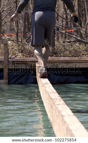 POCONO MANOR, PA - APR 29: A man walks across a narrow beam over water at Tough Mudder on April 29, 2012 in Pocono Manor, Pennsylvania. The course is designed by British Royal troops.