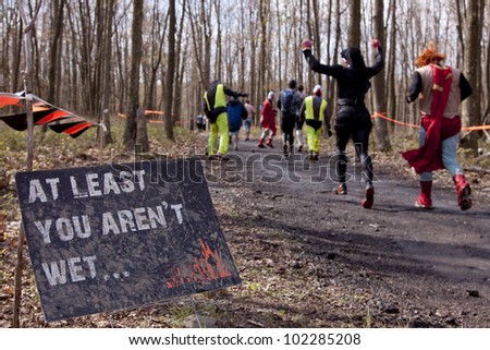 POCONO MANOR, PA - APR 28: Participants run past a sign that reads At Least You Aren't Wet at Tough Mudder on April 28, 2012 in Pocono Manor, Pennsylvania. British Royal troops designed the course.
