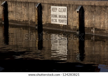 A sign posted above the water line at a city dock that warns boaters to Keep Clear - Docking, Unloading, Holding Prohibited.