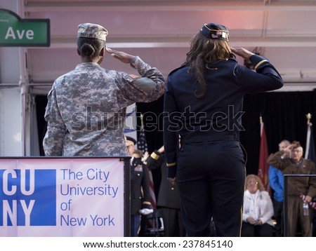 NEW YORK - NOV 11, 2014: Two female US veterans salute from the CUNY float as it passes the VIP stage during the 2014 America\'s Parade held on Veterans Day in New York City on November 11, 2014.