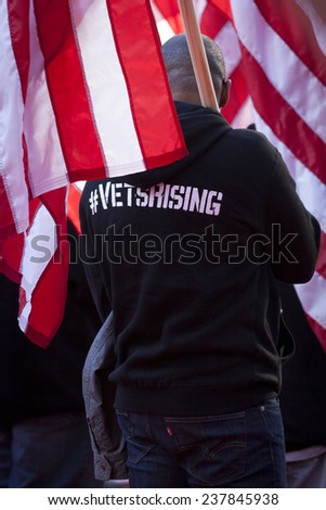 NEW YORK - NOV 11, 2014: A US vet wearing a hoodie that says #VetsRising carries the American Flag in the 2014 America\'s Parade held on Veterans Day in New York City on November 11, 2014.