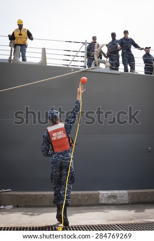 STATEN ISLAND, NY - MAY 20 2015:  A sailor from NWS Earle Port Services throws a line to personnel of guided-missile destroyer USS Barry (DDG 52) as the ship docks at Sullivans Pier for Fleet Week NY.
