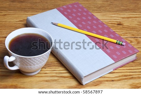 Coffee and a book waiting to be opened, a pencil waiting to take notes, all sitting on a beautiful wood table