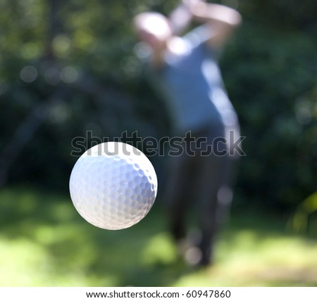 A golf ball just coming off the tee from a golfer in swing.