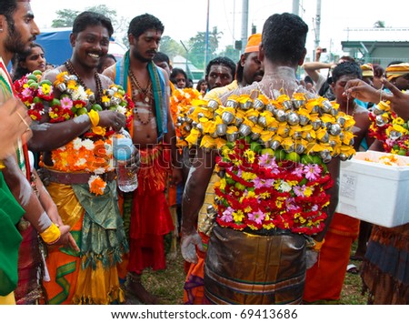 BATU CAVE, MALAYSIA - JAN 20 : An experienced man decorating a hindu devotee\'s body with dozens of tiny milk pots and flowers during Thaipusam on January 20, 2011 at Batu Cave temple, Malaysia.