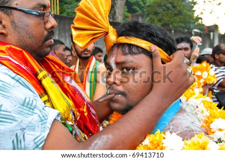 BATU CAVE, MALAYSIA - JAN 20 : A man is putting a hair band onto a devotee\'s head during Thaipusam on January 20, 2011 at Batu Cave temple, Malaysia.