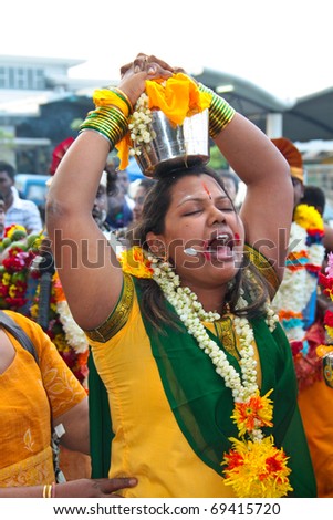 BATU CAVE, MALAYSIA - JAN 20 : Woman carrying big pot of milk with her tongue pierced during Thaipusam on January 20, 2011 at Batu Cave temple, Malaysia.