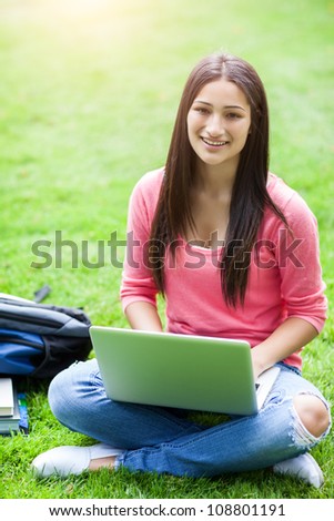 A shot of a hispanic college student sitting on the grass working on laptop at campus