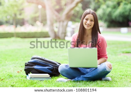 A shot of a hispanic college student sitting on the grass working on laptop at campus