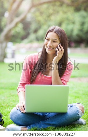 A beautiful hispanic college student talking on the phone working on her laptop on campus