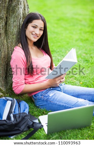 A shot of a hispanic college student sitting on the grass studying