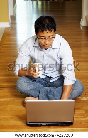 An asian businessman sitting on the floor and working on his laptop at home