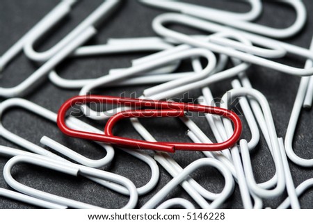 A red paper clip on top of white paper clips