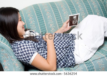 A pregnant woman lying down on a sofa looking at the ultrascan of her unborn child