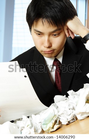 A shot of a stressed asian businessman working hard in the office with paper all over the table