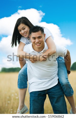A happy asian couple doing piggyback ride outdoor in a park