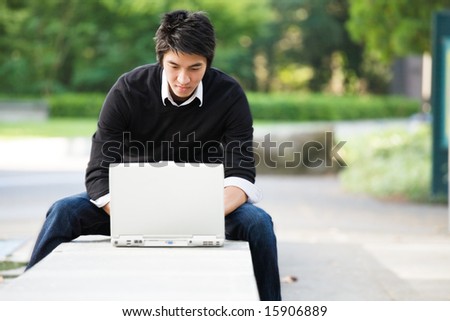 A shot of an asian student working on his laptop at the campus