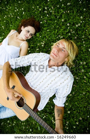 A happy caucasian couple playing guitar at a park