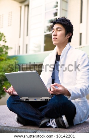 An asian college student doing meditation while holding a laptop